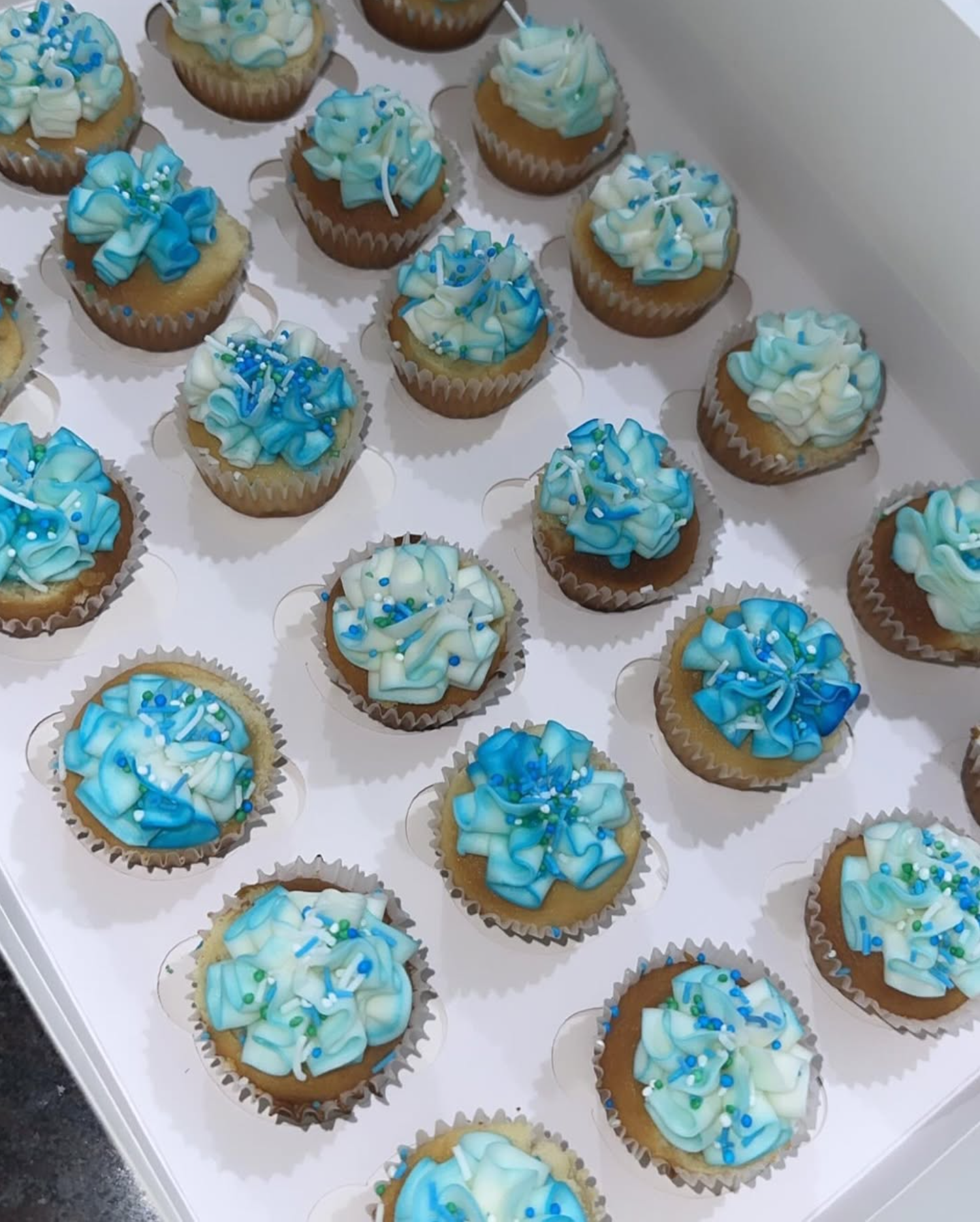 Tray of handmade vanilla cupcakes with blue and white buttercream swirls and sprinkles by Sugar Sweet Bakery